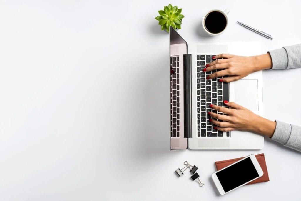 Person typing on a laptop with a coffee cup and plant nearby.