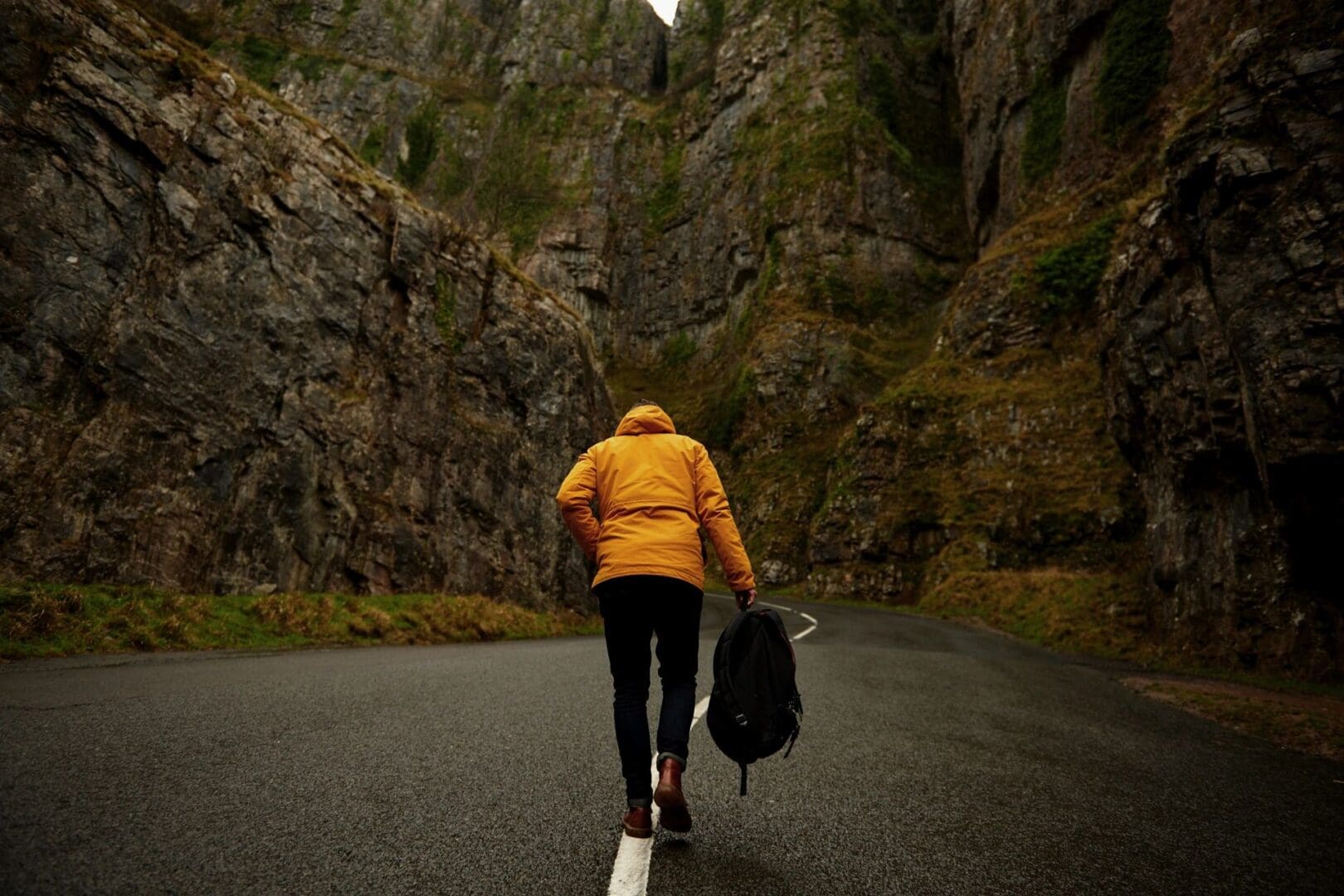 Person in a yellow jacket walking on a road through a rocky canyon.