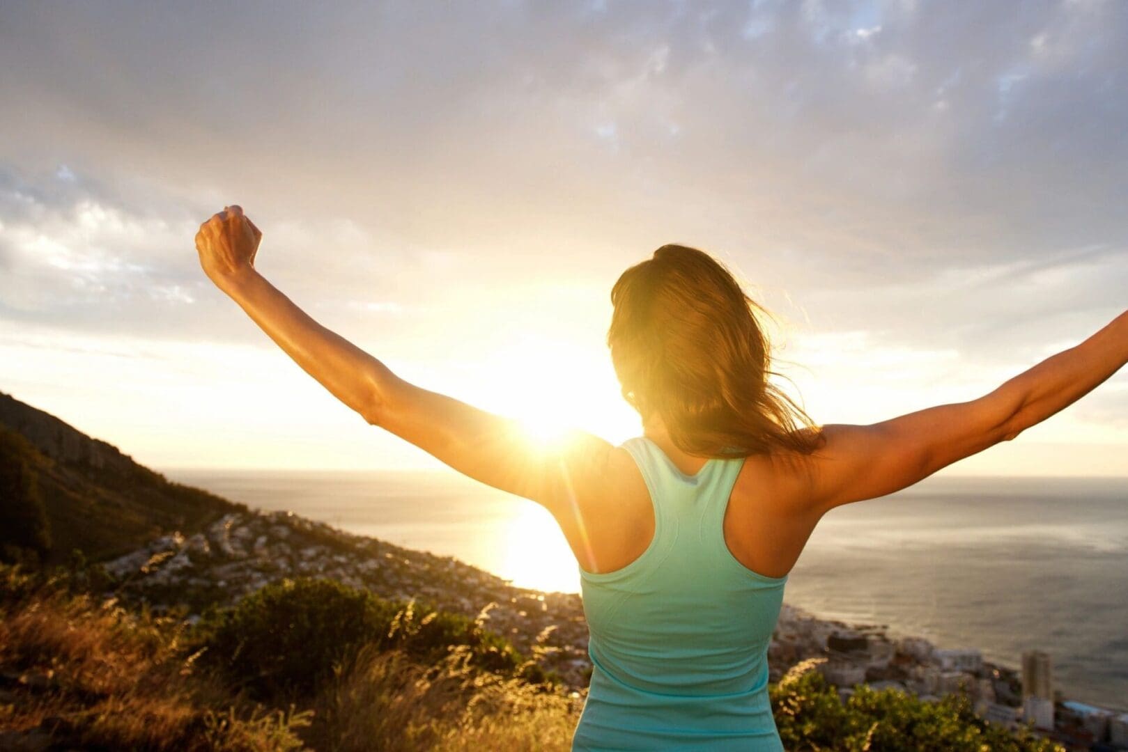 Woman celebrating outdoors at sunrise with arms raised.